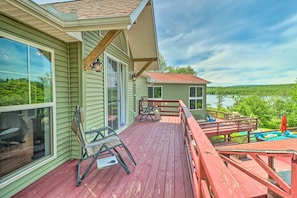 A wooden deck with outdoor furniture, a glass door, and a view of a lake.