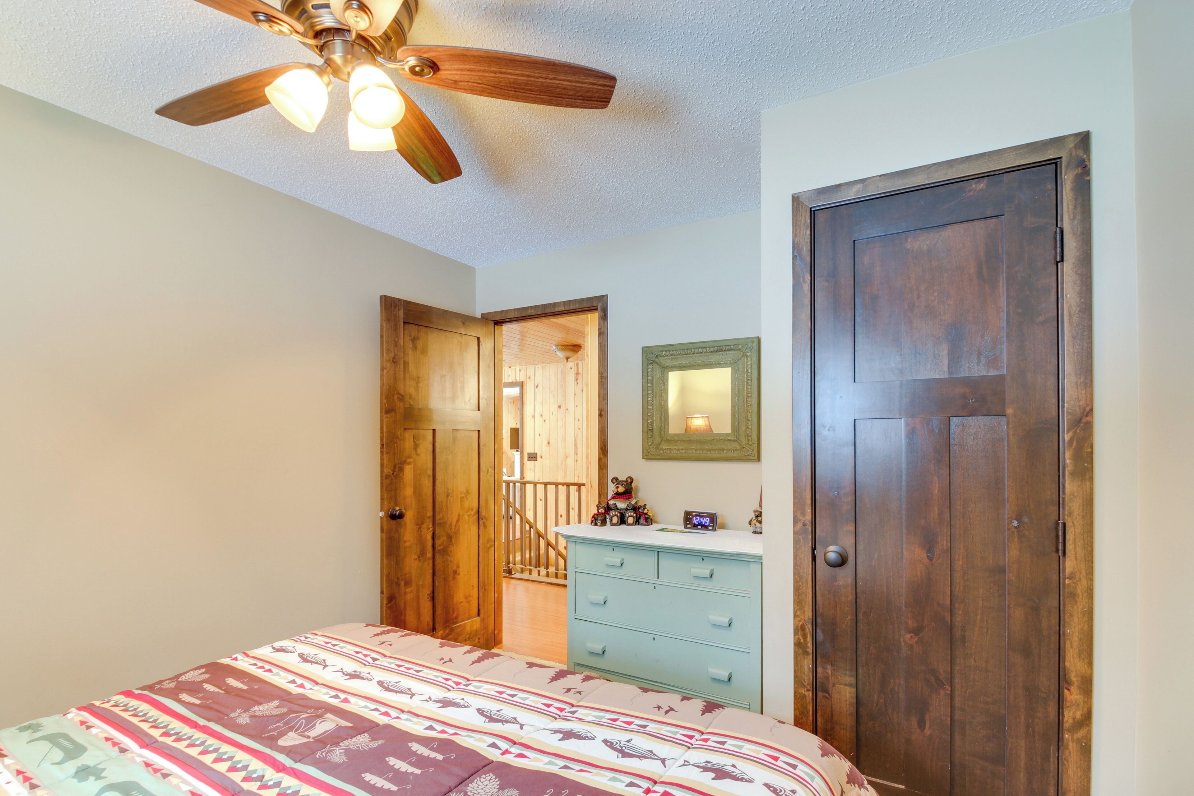 A bedroom with a bed, a dresser, a wooden door, a ceiling fan, and a staircase leading to another room.