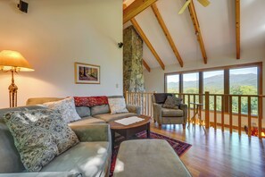 A spacious living room with a large sofa, a coffee table, and a view of the outdoors through large windows. - Architect-designed Franconia Home: Hot Tub & Views (Franconia)