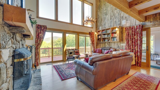 A spacious living room with a stone fireplace, leather sofa, and a large bookshelf. - Architect-designed Franconia Home: Hot Tub & Views (Franconia)