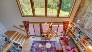A cozy room with a large window, a fireplace, a bookshelf, and a comfortable seating area. - Architect-designed Franconia Home: Hot Tub & Views (Franconia)