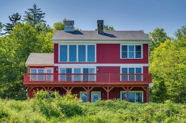 A two-story house with a red exterior, multiple windows, and a balcony. - Architect-designed Franconia Home: Hot Tub & Views (Franconia)