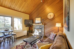 A cozy living room with a stone fireplace, wooden ceiling, and a large clock. - Breathtaking Bend Condo w/ Resort Amenities! (Bend)