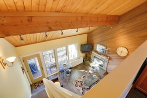 A spacious living area with a high ceiling, a fireplace, a television, and a clock on the wall. - Breathtaking Bend Condo w/ Resort Amenities! (Bend)