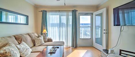 A hotel room with a sofa, a wooden coffee table, a TV, and a balcony with curtains.
