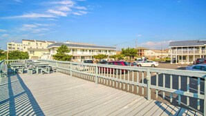 A wooden boardwalk with picnic tables and a parking area with cars. - Beautiful Brigantine Condo - Walk to Beach! (Brigantine)