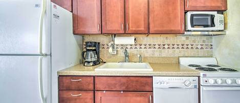 Una cocina funcional con un refrigerador blanco, un microondas, una cafetera, un fregadero y un lavavajillas.