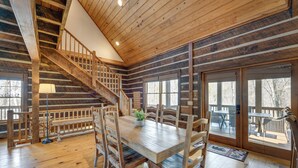 A spacious wooden cabin interior with a dining area, a staircase, and large windows.