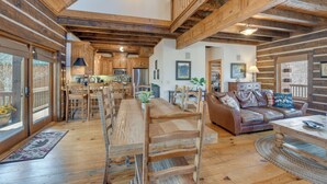 A spacious living area with a wooden dining table, a leather sofa, and a kitchen in the background.