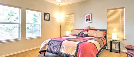 Une chambre à coucher avec un lit, un ventilateur de plafond, une table de chevet et une fenêtre avec des stores.