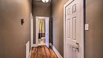 A hallway with a wooden floor, a white door on the right, and a bathroom visible through an open door at the end.