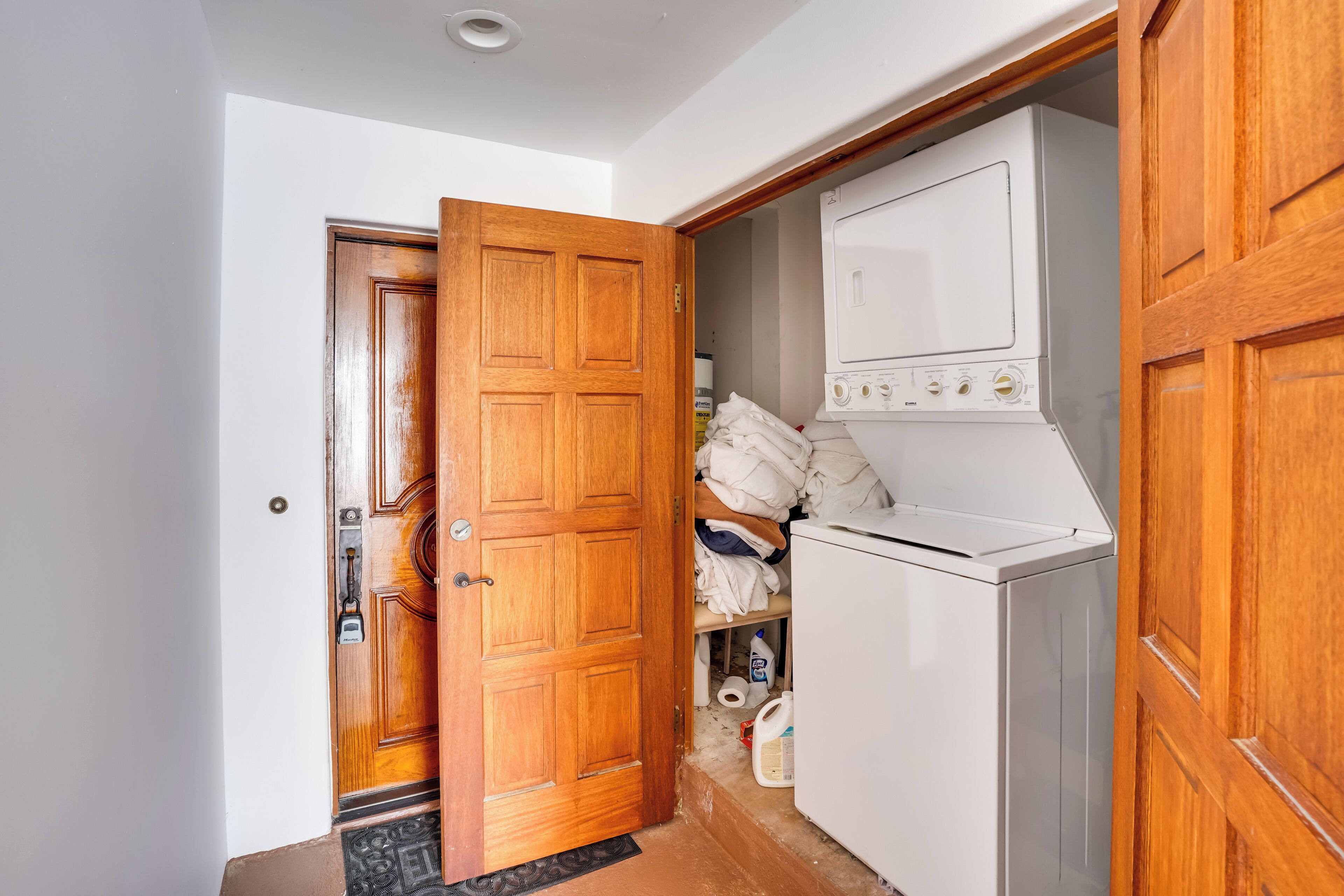A laundry room with a washing machine and dryer, wooden doors, and a shelf with folded clothes.