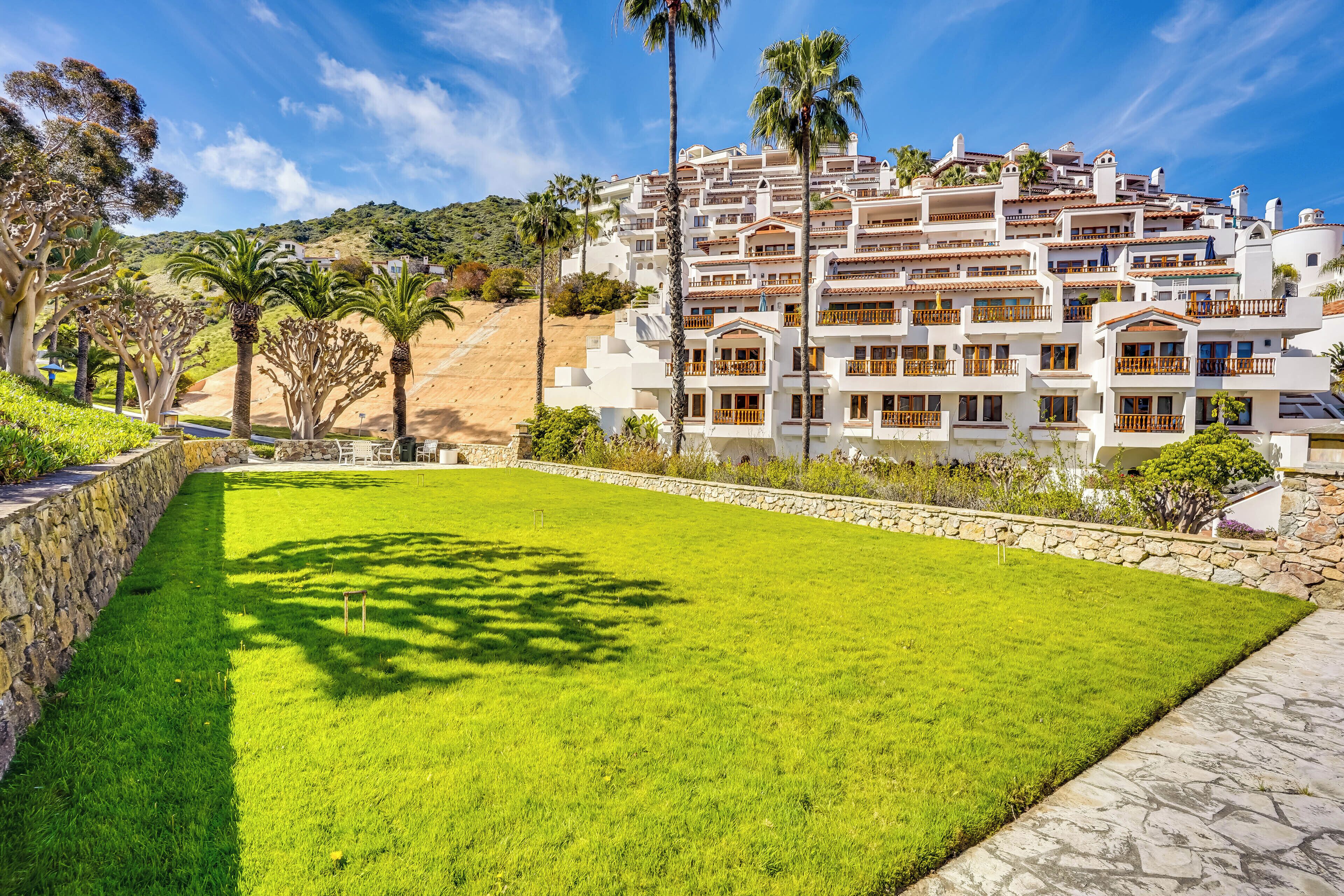 Un hotel con varios balcones, un césped bien cuidado y un muro de piedra de contención.