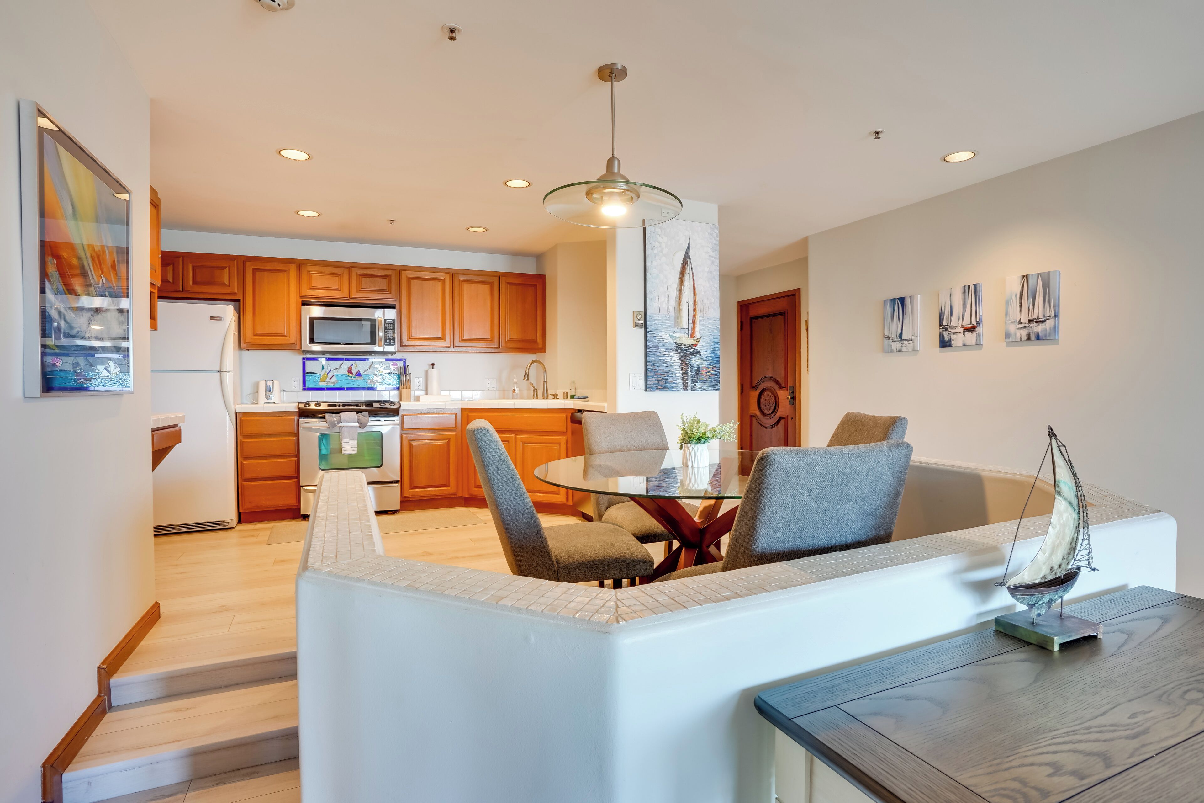 A modern kitchen with wooden cabinets, a microwave, and a dining area with a glass table and chairs.