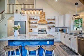 Een moderne keuken met een groot eiland, barstoelen en een hangende lamp.