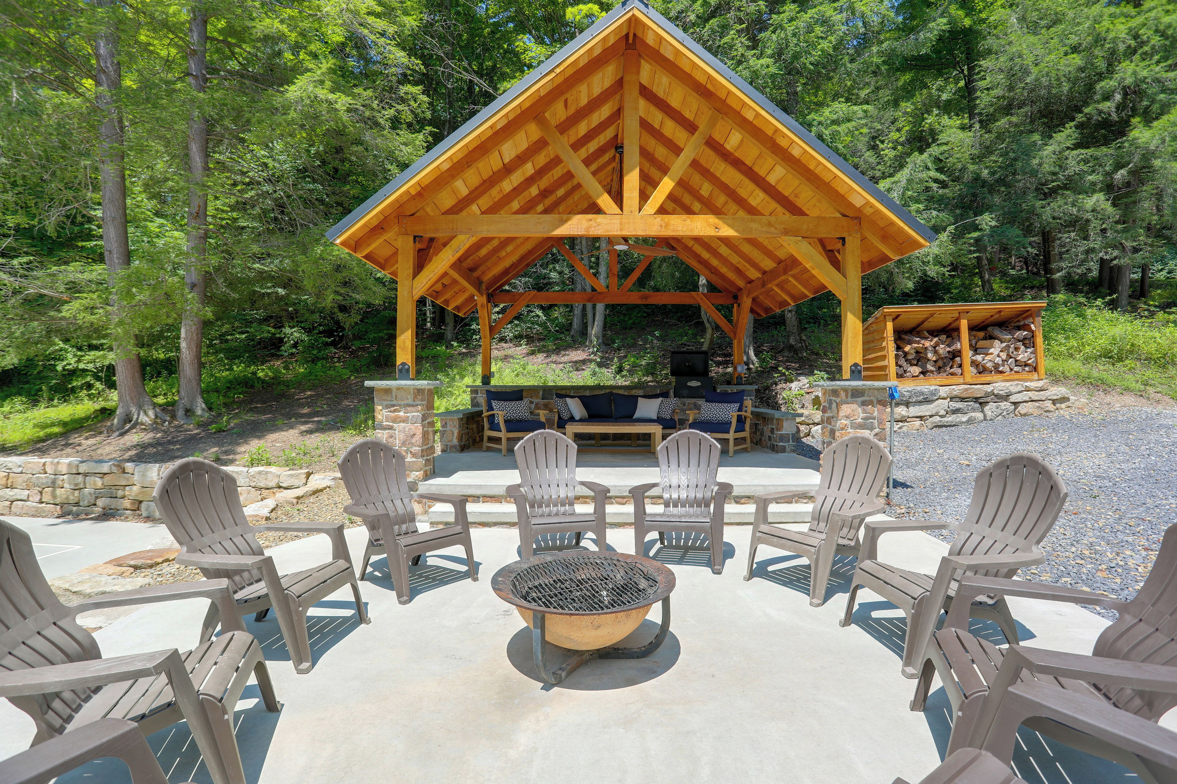 A wooden gazebo with a fire pit and seating area surrounded by Adirondack chairs.