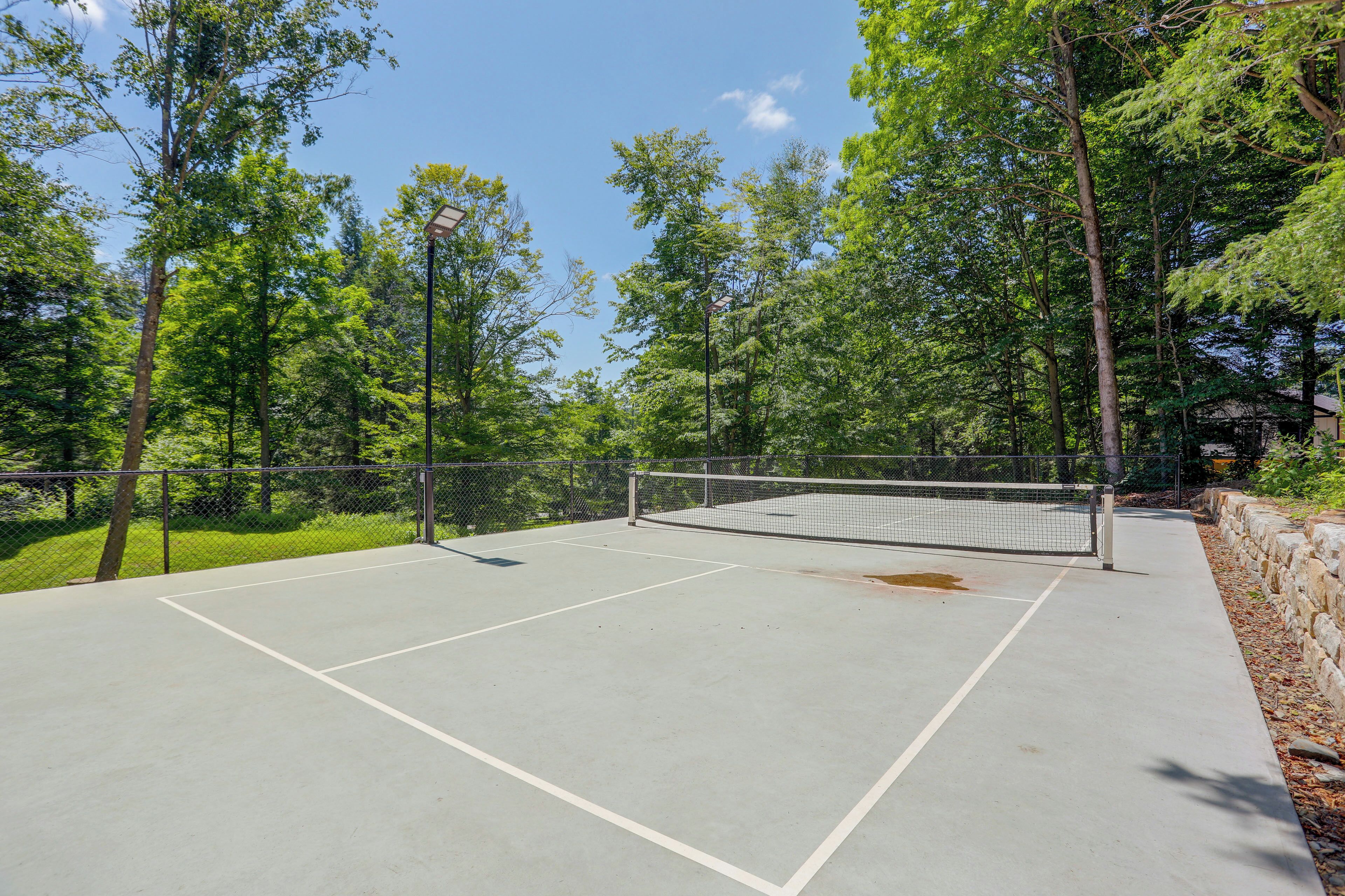 An outdoor tennis court surrounded by trees and a stone wall.