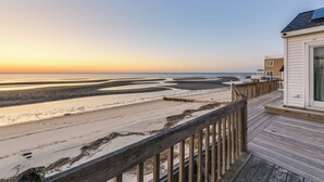 A wooden deck leading to a white building with a glass door, overlooking a beach with sand and water. - Delaware Bay & Sunset Views: Cape May Cottage (Cape May Court House)