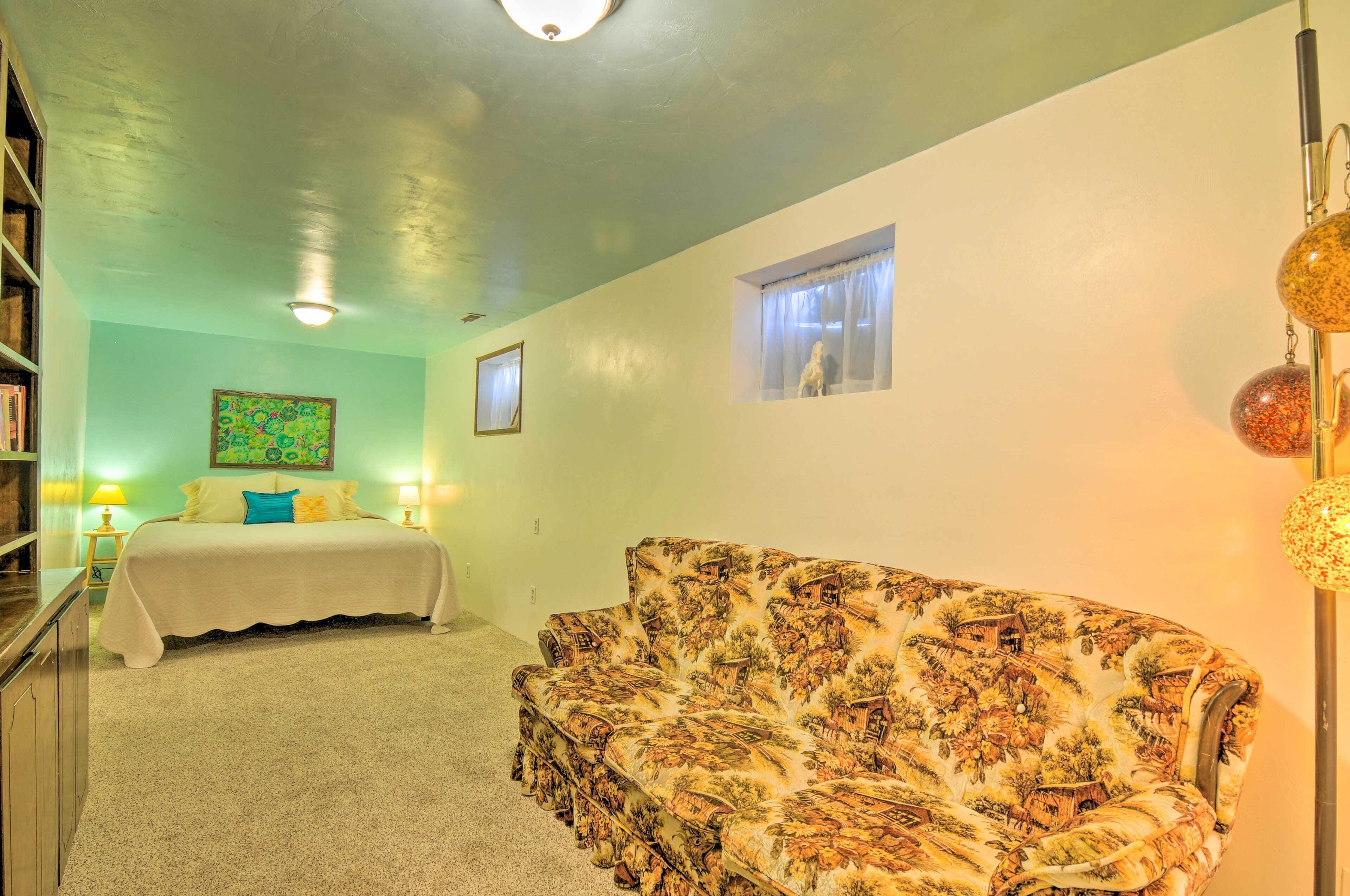 A bedroom with a bed, a patterned sofa, a small window, and a bookshelf.