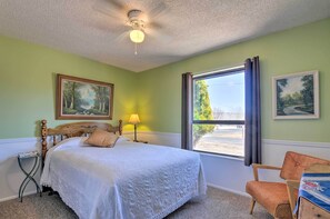 Un dormitorio con cama, una silla, un ventanal con cortinas y dos cuadros en la pared.