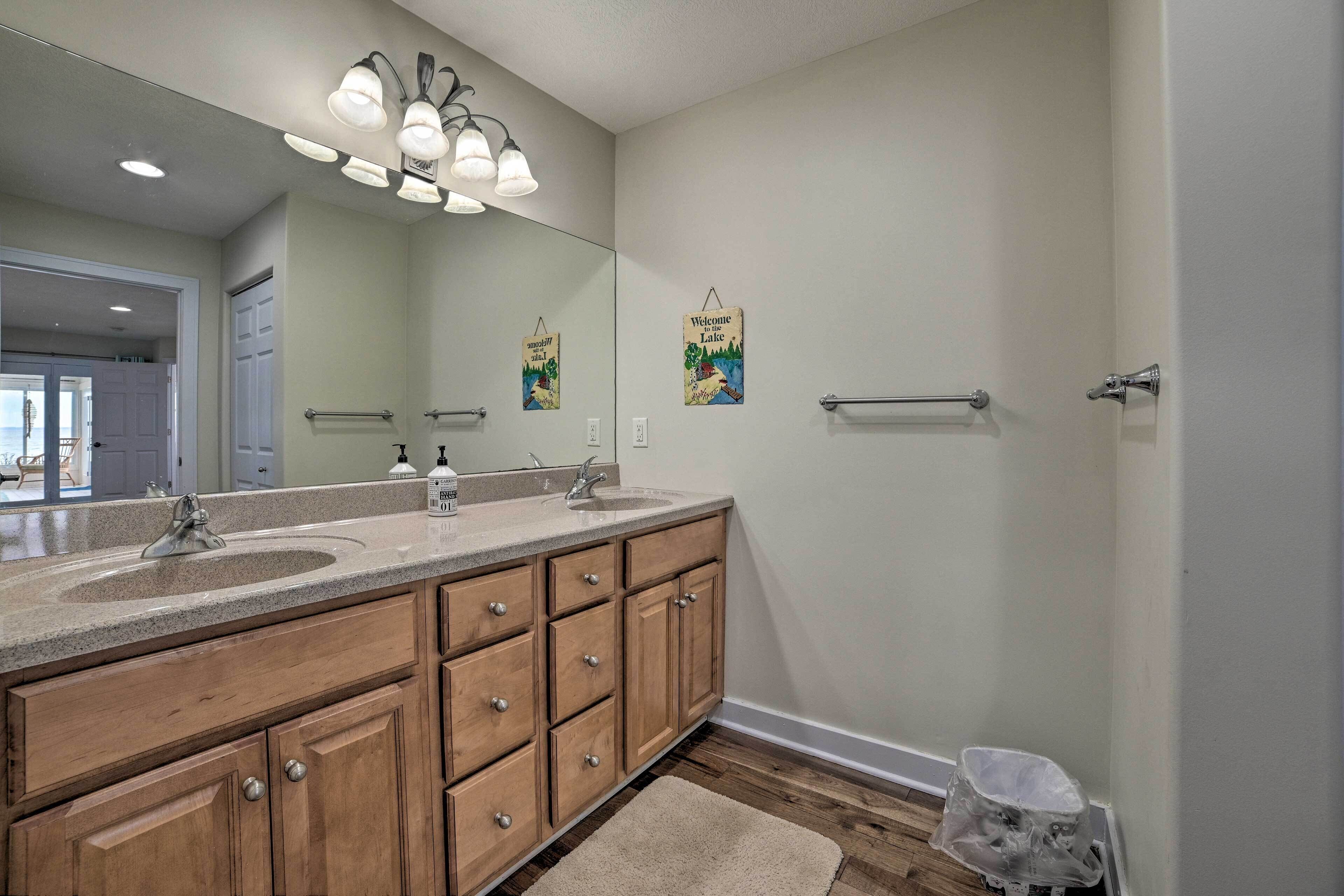 A bathroom with a double vanity, a large mirror, a towel rack, and a welcome sign.