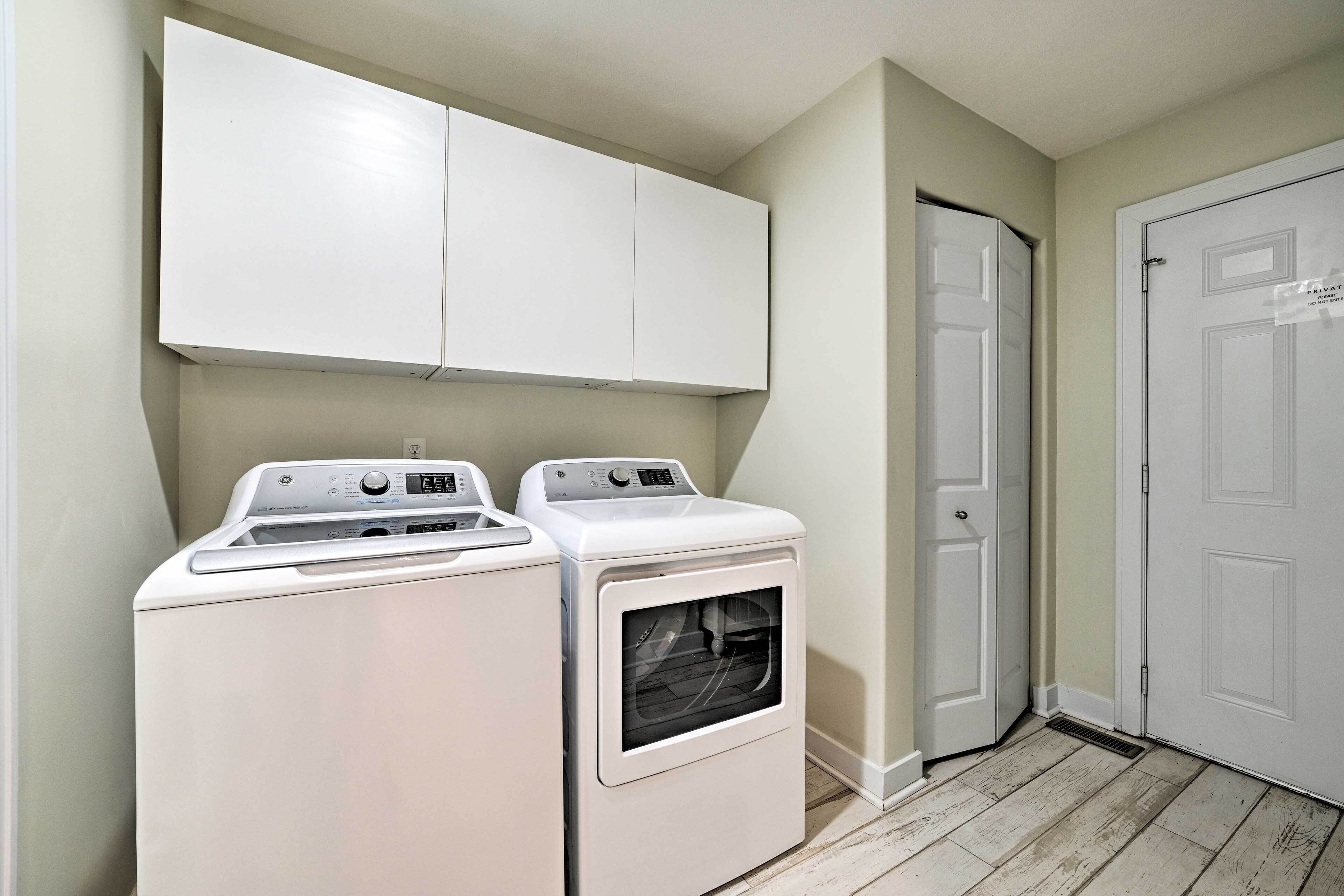 A laundry room with two white appliances, a cabinet above, and a door to the right.