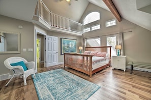 A spacious bedroom with a wooden bed, a white chair, and a large window. - Spacious, Peaceful Lake House w/ Sandy Beach (Northport)