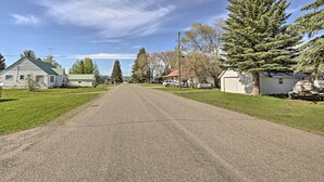 A rural road with houses on either side, a clear sky, and a large evergreen tree. - Ashton Escape w/ Yard: 56 Mi to West Yellowstone! (Ashton)