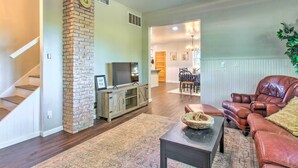 A living room with a brick fireplace, a TV, a leather couch, and a dining area in the background. - Beautifully Restored Farmhouse in Marshall! (Martinsville)