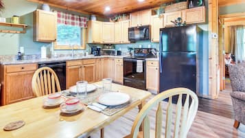 Una cocina de madera con una mesa de comedor para cuatro personas, un refrigerador, microondas y estufa.
