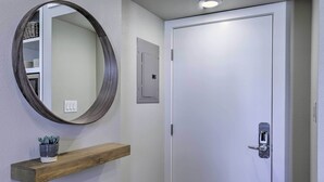 A white door with a silver handle, a round mirror on the wall, and a wooden shelf with a potted plant.
