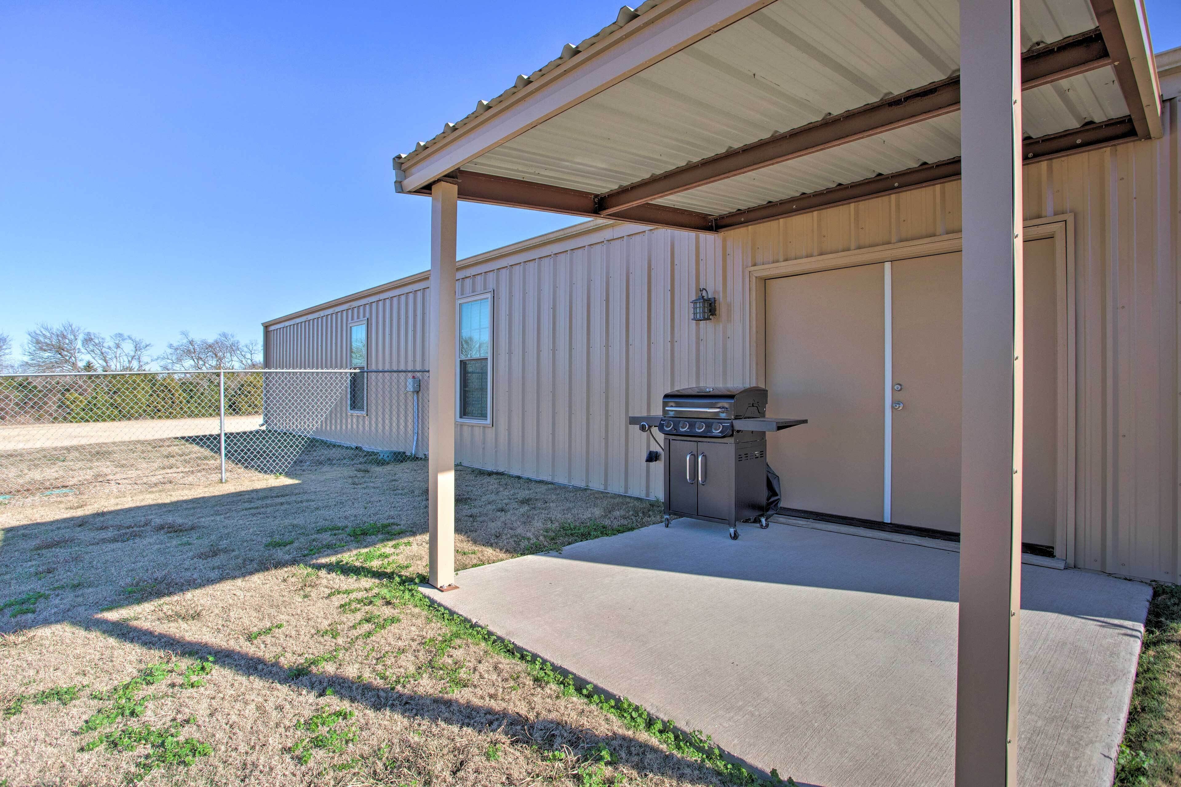 A covered outdoor area with a barbecue grill, a concrete patio, and a building with a garage door.