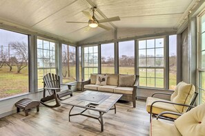 Ein Wintergarten mit großem Fenster, Deckenventilator, einer Couch, einem Sessel und einem Couchtisch.