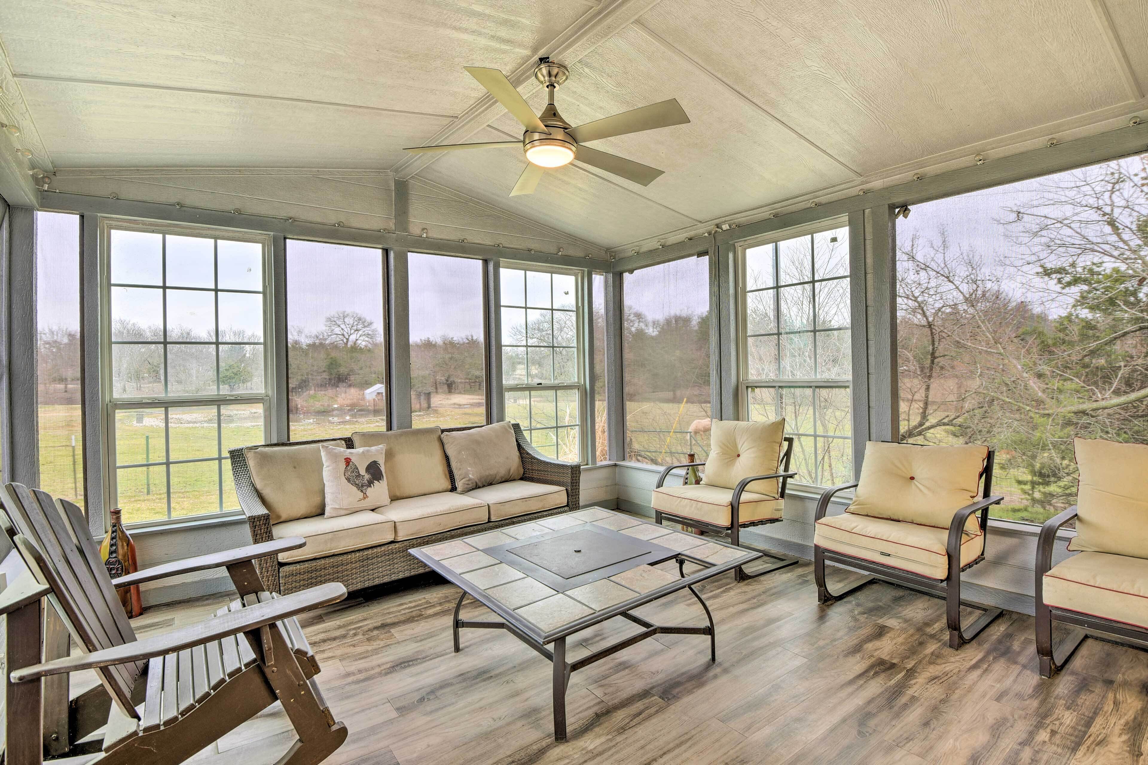 A covered patio with a ceiling fan, large windows, a sofa, chairs, and a coffee table.