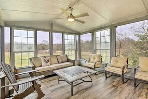 Eine überdachte Terrasse mit Deckenventilator, großen Fenstern, einer Couch, Stühlen und einem Couchtisch.