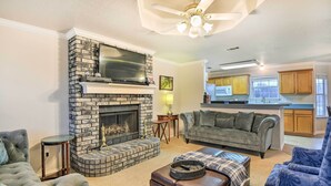 A living room with a fireplace, a sofa, a coffee table, and a kitchen in the background. - Blue Ridge Vacation Rental w/ Game Room! (Blue Ridge)