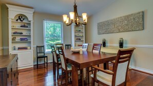 A dining room with a wooden table and chairs, surrounded by bookshelves and a chandelier. - Charlotte Vacation Rental w/ Private Hot Tub! (Charlotte)