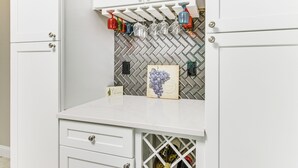 A kitchen with white cabinets, a herringbone tile backsplash, a wine rack with glasses, and a wine bottle storage unit. - Charlotte Vacation Rental w/ Private Hot Tub! (Charlotte)