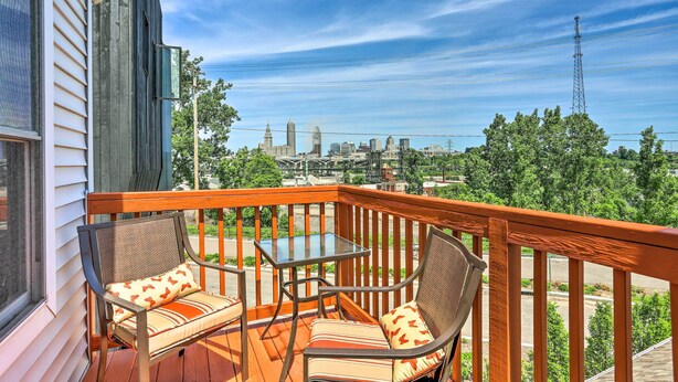 Une terrasse en bois avec deux chaises et une table, d’où l’on peut admirer une vue sur la ville, avec ses bâtiments et un pylône de ligne électrique.