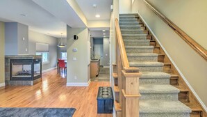Un vaste espace de vie doté de planchers en bois franc, d’une cheminée, d’un escalier avec des rampes en bois et d’une vue sur la cuisine.