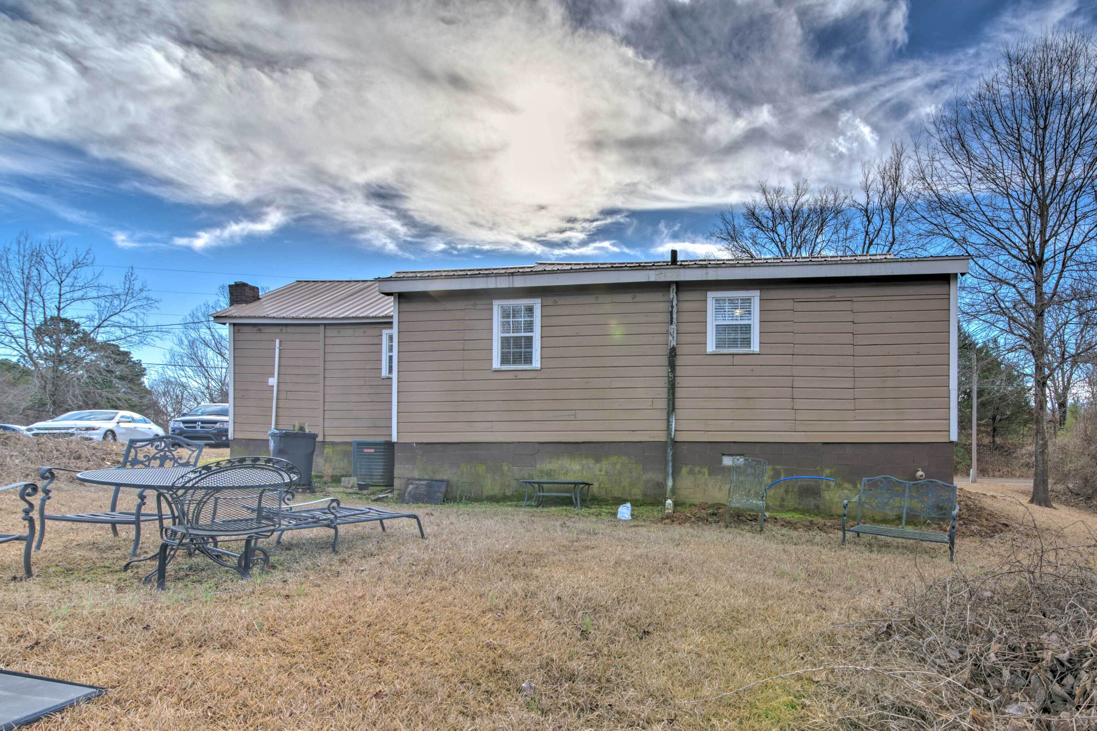 A two-story house with a brown exterior, a small front yard with a metal table and benches, and a clear sky with clouds.