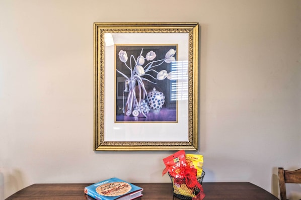 A framed artwork on a wall, a table with a book and a basket of snacks. - Charming Oxford Home ~ 7 Mi to Ole Miss! (Oxford)