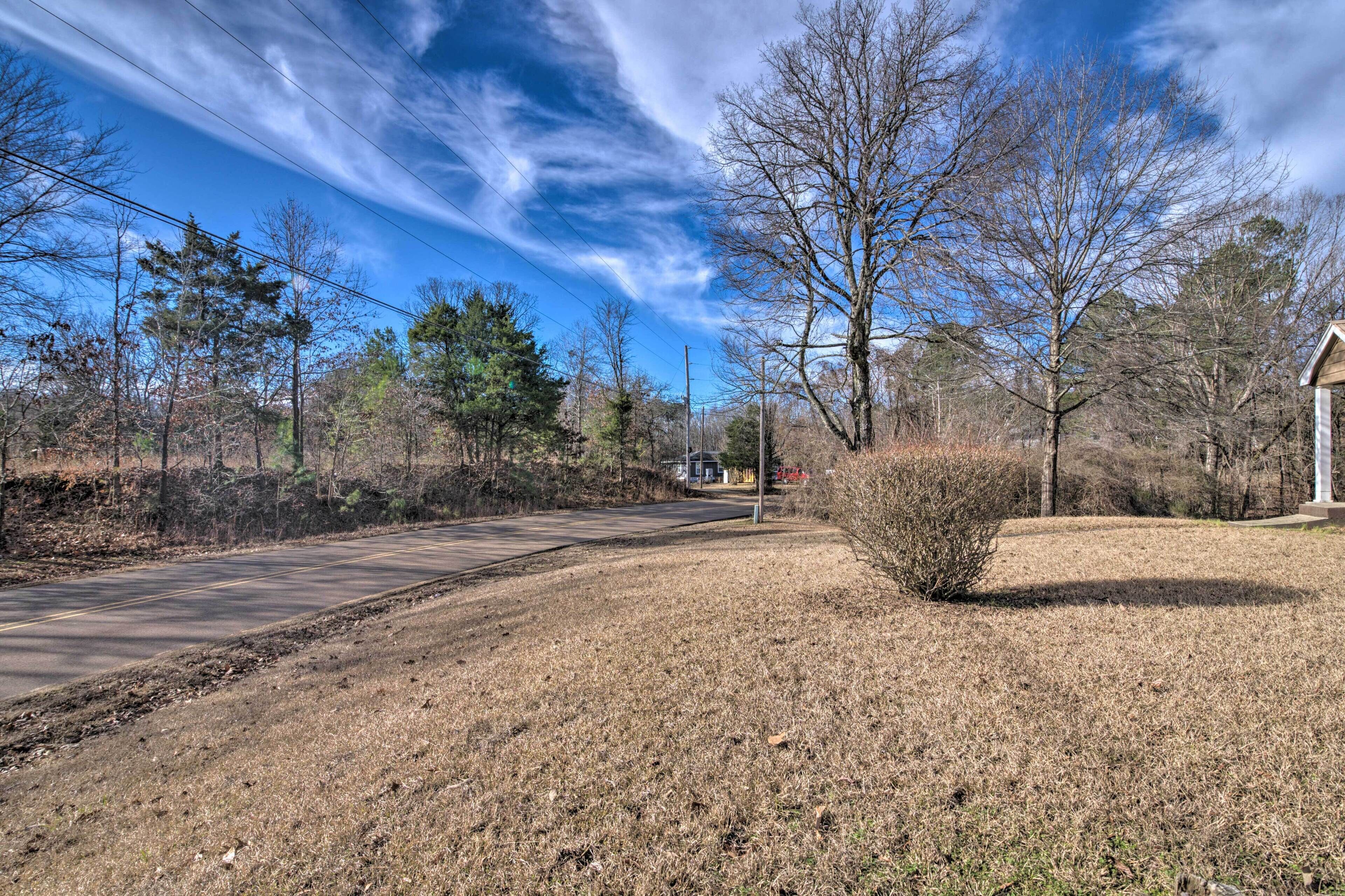 A rural road with a clear sky, surrounded by trees and a grassy area.