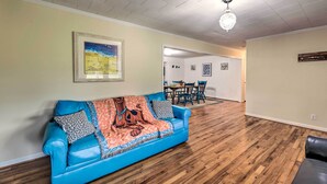 A living room with a blue sofa, wooden flooring, a chandelier, and a dining area in the background. - Coastal Retreat! Harkers Island Boating Base (Harkers Island)