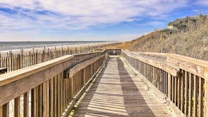 Ein hölzerner Steg führt zu einem Strand, begleitet von einer Holzzahlung auf einer Seite und einem Gebäude auf der anderen.