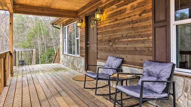A wooden porch with two chairs and a small table, a stone wall, and a door with a window.