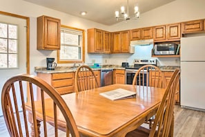 A kitchen with wooden cabinets, a dining table, chairs, a coffee maker, a microwave, a stove, and a refrigerator.