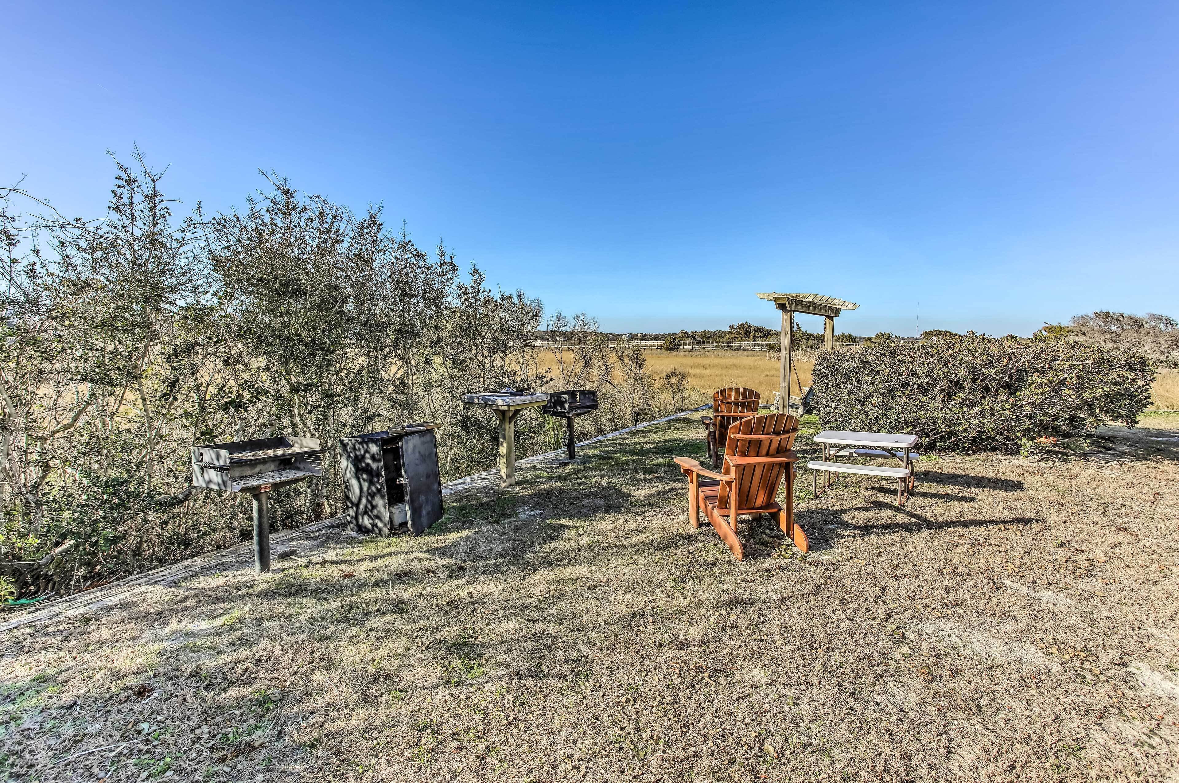 Un área de picnic con una mesa y sillas de madera, una parrilla y un comedero para pájaros.
