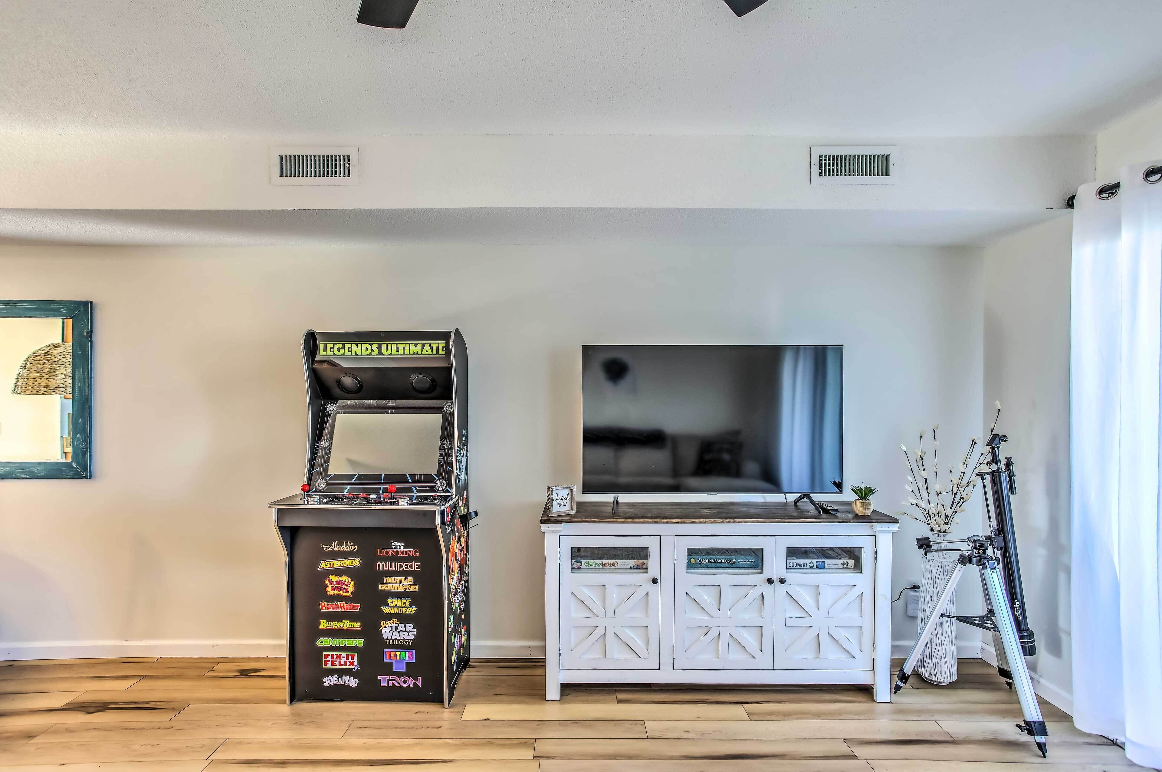 A room with a gaming machine, a television, and a tripod.
