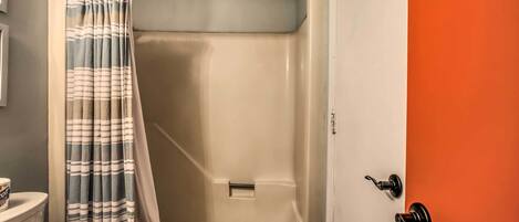 Un baño con ducha, inodoro y puerta con manija.